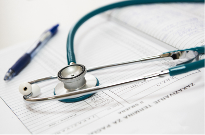 A stethoscope rests on open medical charts, accompanied by a blue pen. The setting conveys a clinical atmosphere, emphasizing healthcare and documentation.