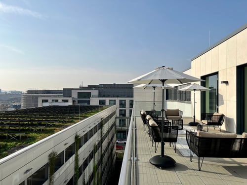 Dachterrasse mit Sitzmöbeln und Sonnenschirmen, Blick auf grüne Dächer.