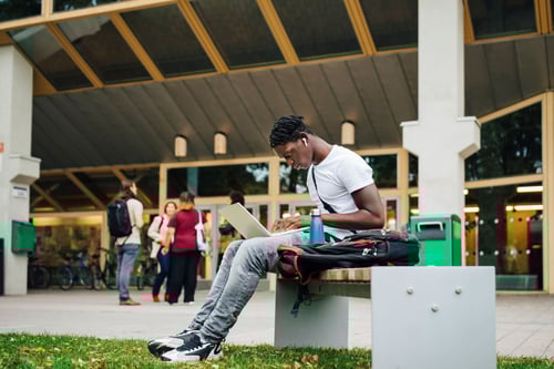 Young man looking at laptop sitting outside building