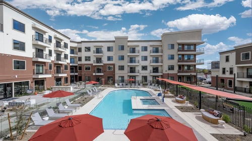 swimming pool with lounge chairs and umbrellas in front of a building at Icon @ Cooley Station, Gilbert, AZ