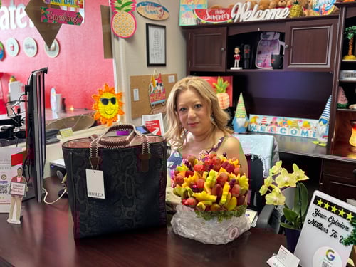 Female team member sitting at brown desk that is decorated for her birthday with a fruit bouquet and a brown and black purse on desk.