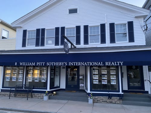 White building with navy blue storefront and black shutters housing William Pitt Sotheby's International Realty in Essex, Connecticut, featuring large display windows with property listings.