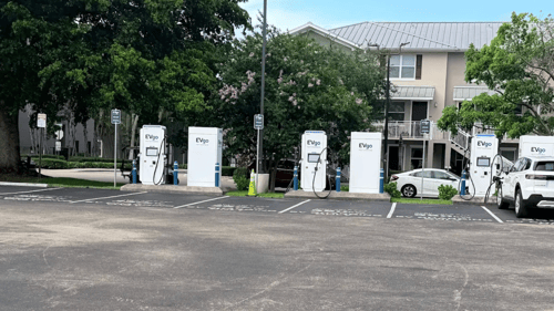 Several EVgo fast charging units installed in marked parking spaces at a public charging station, with EVgo logos on the chargers, protective bollards around each unit