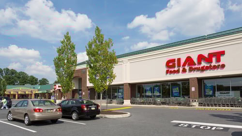 Black car and tan car parked in front of Giant Food & Drugstore with two trees to the side