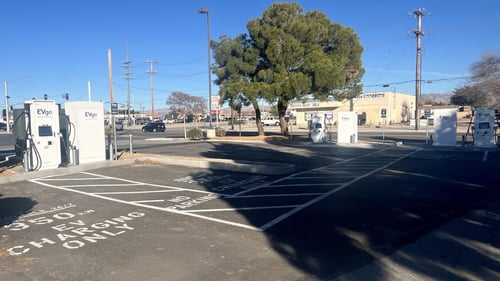 Several EVgo fast-charging units installed in marked parking spaces at a public charging station, with EVgo logos on the chargers, protective bollards around each unit
