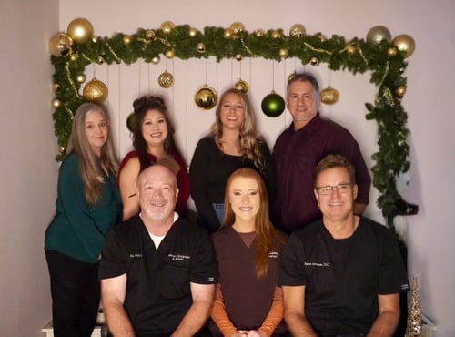 The doctors and staff of the Hurst and Fort Worth locations of Absolute Chiropractic & Rehab sitting on a bench in front of office Christmas decorations.