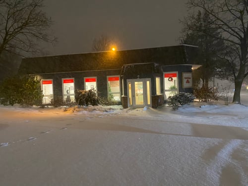Brick building at night with lights shining through windows and snow on the ground