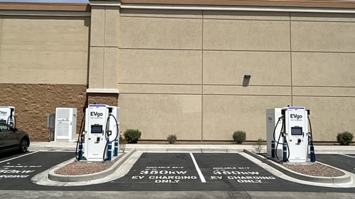 Several EVgo fast-charging units installed in marked parking spaces at a public charging station, with EVgo logos on the chargers, protective bollards around each unit