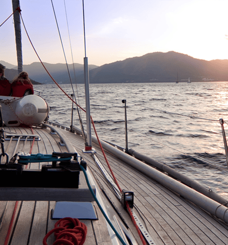 On-deck view of a sailboat on the ocean during sunset.