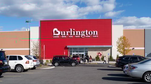 Black SUV driving past front entrance of Burlington through a full parking lot