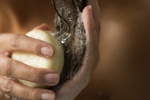A hand is holding a shampoo bar and lathering up their hair.