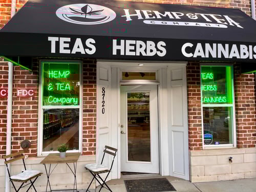 Exterior of Hemp & Tea Company in Charlotte, NC with neon signs and patio seating.
