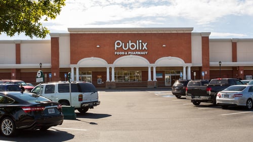 Two rows of parked cars in front of Publix at Shops of Huntcrest shopping center, tree on the left