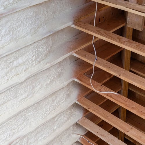 Closed-cell spray foam insulation applied between wall studs in a wooden frame wall.