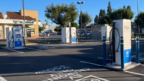 Several EVgo fast-charging units installed in marked parking spaces at a public charging station, with EVgo logos on the chargers, protective bollards around each unit
