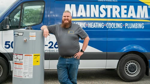 A plumber from Mainstream standing with a water heater in front of the company truck