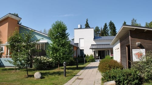 Ulkokuva Kaskesta. Julkisivu on valkoista kiveä, ja pääovelle johtaa kivitetty pihatie. Sivusiipi on oranssia kiveä ja vaaleansinistä panelointia. Pihatien ympärillä on pensaita ja pieniä puita.