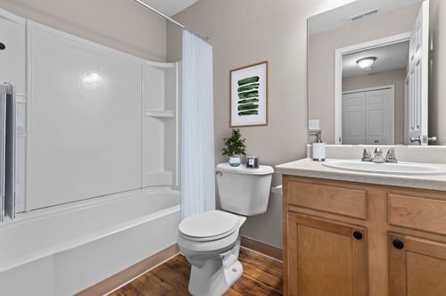 Modern bathroom with tub and shower, oak vanity, and wood-style flooring at Water’s Edge Apartments in South Lyon, MI