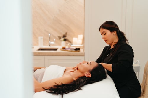 A spa therapist gives a relaxing head massage to a client lying on a treatment bed, surrounded by a serene setting with soft lighting and candles.