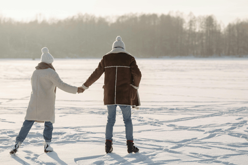 An adult couple skating on a lake in the winter.