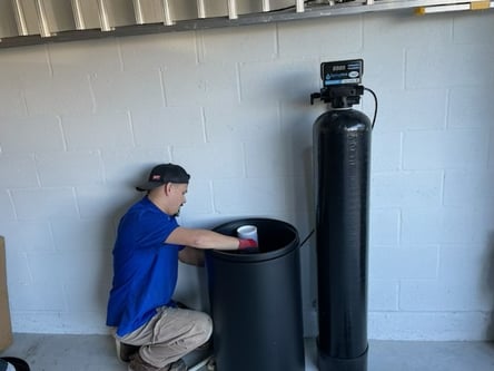 bluefrog plumber kneeling in a garage installing a water softener system