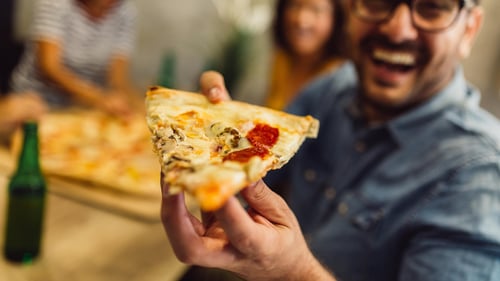 A smiling man holding a pizza slice