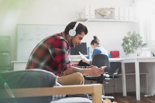 Man with headphones sitting in chair looking at phone