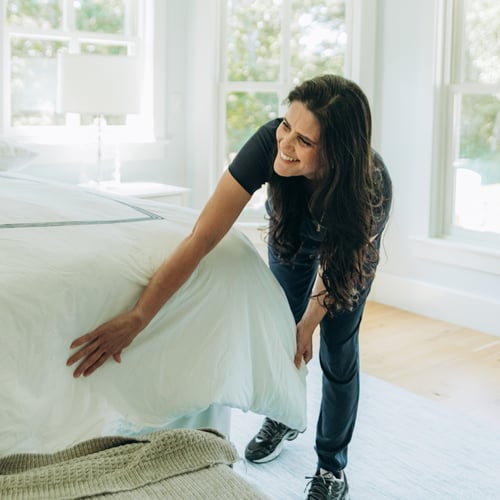 Woman making the bed in a bright, well-lit room.