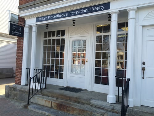 White building with columned entrance and fan window detail housing William Pitt Sotheby's International Realty in Litchfield, Connecticut, featuring doors with glass panes and stone steps with black railings.