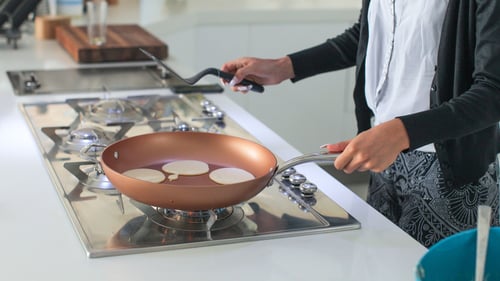 A woman cooks pancakes on an propane stovetop.
