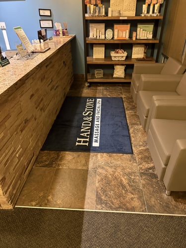 Interior shot of Hand & Stone reception area with branded floor mat and guest seating.