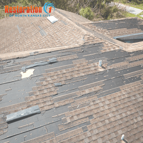 Asphalt shingle roof in Kansas City with missing and wind-damaged shingles after a severe storm.