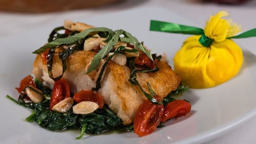 Chilean Sea Bass alla Fiorentina, plated elegantly with sautéed spinach, cherry tomatoes, toasted pine nuts, basil ribbons, and lemon garnish.