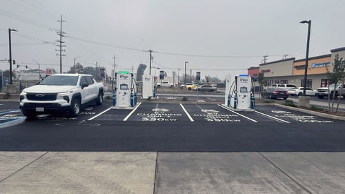 Several EVgo fast-charging units installed in marked parking spaces at a public charging station, with EVgo logos on the chargers, protective bollards around each unit