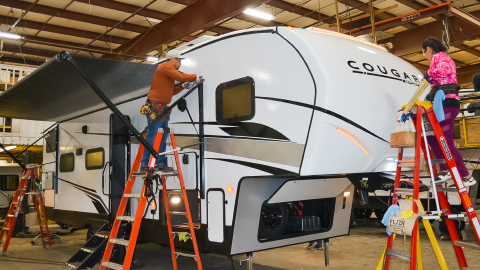 Two workers in a collision bay working on an RV trailer