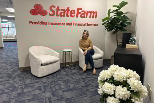 A woman sits thoughtfully in a modern office space with a State Farm logo, surrounded by plush chairs and a decorative plant.