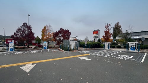 Several EVgo fast-charging units installed in marked parking spaces at a public charging station, with EVgo logos on the chargers, protective bollards around each unit