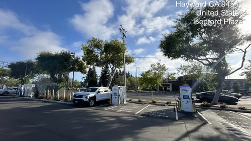 Several EVgo fast charging units installed in marked parking spaces at a public charging station, with EVgo logos on the chargers, protective bollards around each unit