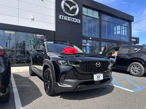 Black Mazda CX-50 SUV with a red bow parked in front of Colonial Mazda dealership in Danbury, CT
