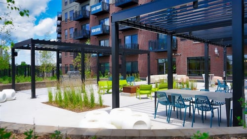 A patio area with tables and chairs is surrounded by a building at The Bessemer at Seward Commons, Minneapolis, MN, 55404
