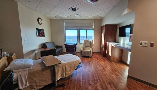 A view of the labor and delivery room with a bed, recliner, sofa and window.