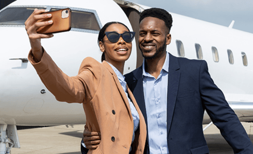 young couple taking a selfie in front of a private plane
