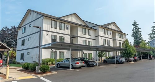 A large white building with a grey roof and a parking lot in front at Sandyplace Apartment Homes, Oregon, 97055