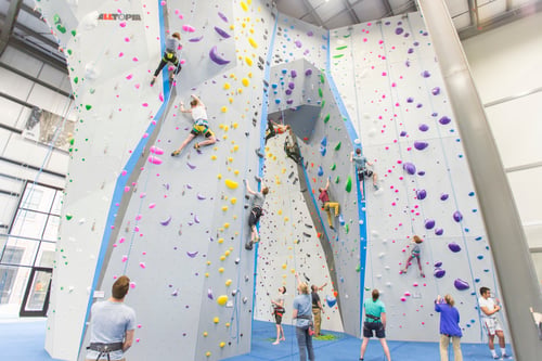 A photo of Central Rock Gym Buffalo's lead climbing archway. People are top rope and lead climbing on the arch and the pillars on both sides.