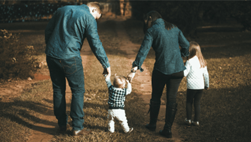 A family of four walking down a grass led path.