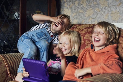Kids laughing on a couch watching a tablet