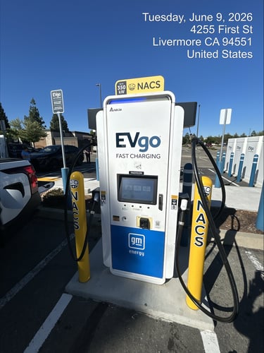NACS EVgo fast charging unit installed in marked parking space at a public charging station, with EVgo logos on the charger,  and yellow protective bollards around the unit