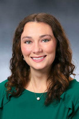 Christine Dumm, PA-C smiling in front of a gray backdrop with a dark green blouse.