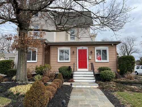 Tan siding on a house with red door and tree out front