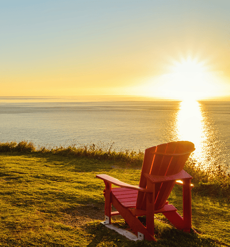 A red adirondack chair placed on lush green grass, during sunset, with a calm lake in the background.